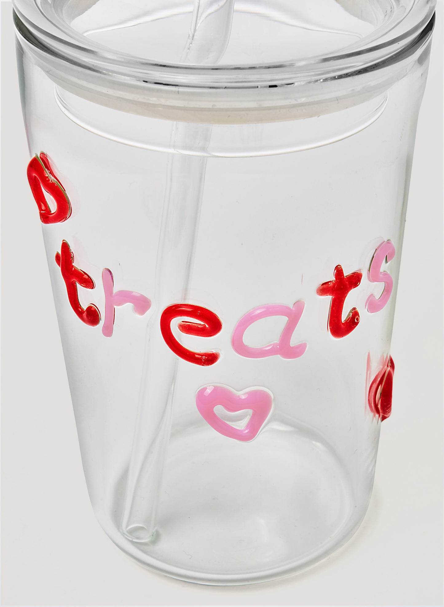Clear glass tumbler with colourful text saying 'treats' and heart designs on a white background