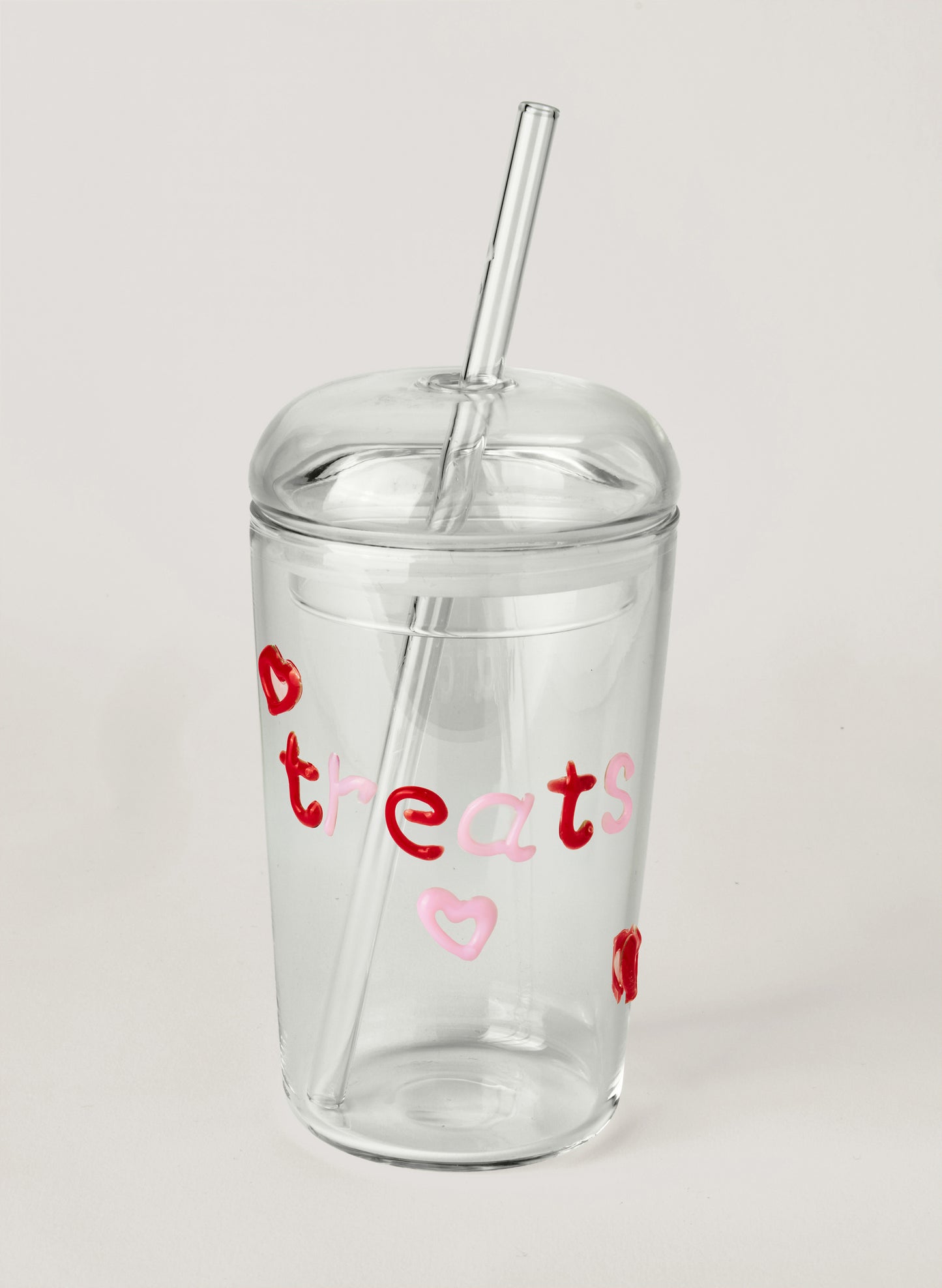 Clear glass tumbler with colourful text saying 'treats' and heart designs on a white background