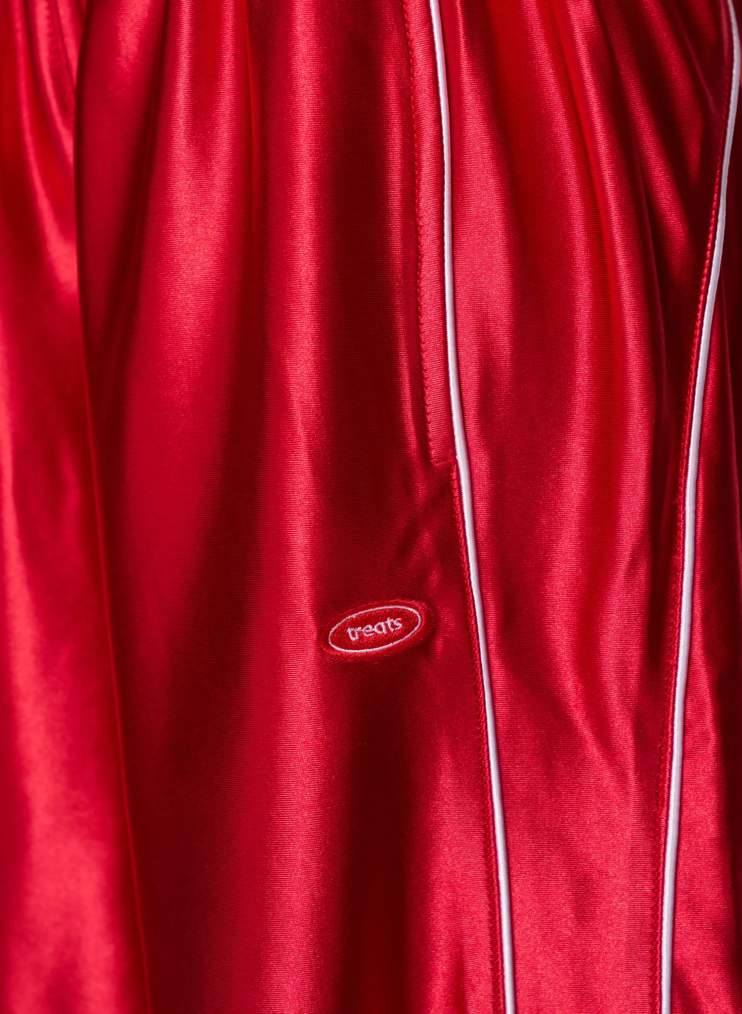 Close-up of a red satin or silk-like garment with white piping and a small oval 'paqos' logo patch near the center.