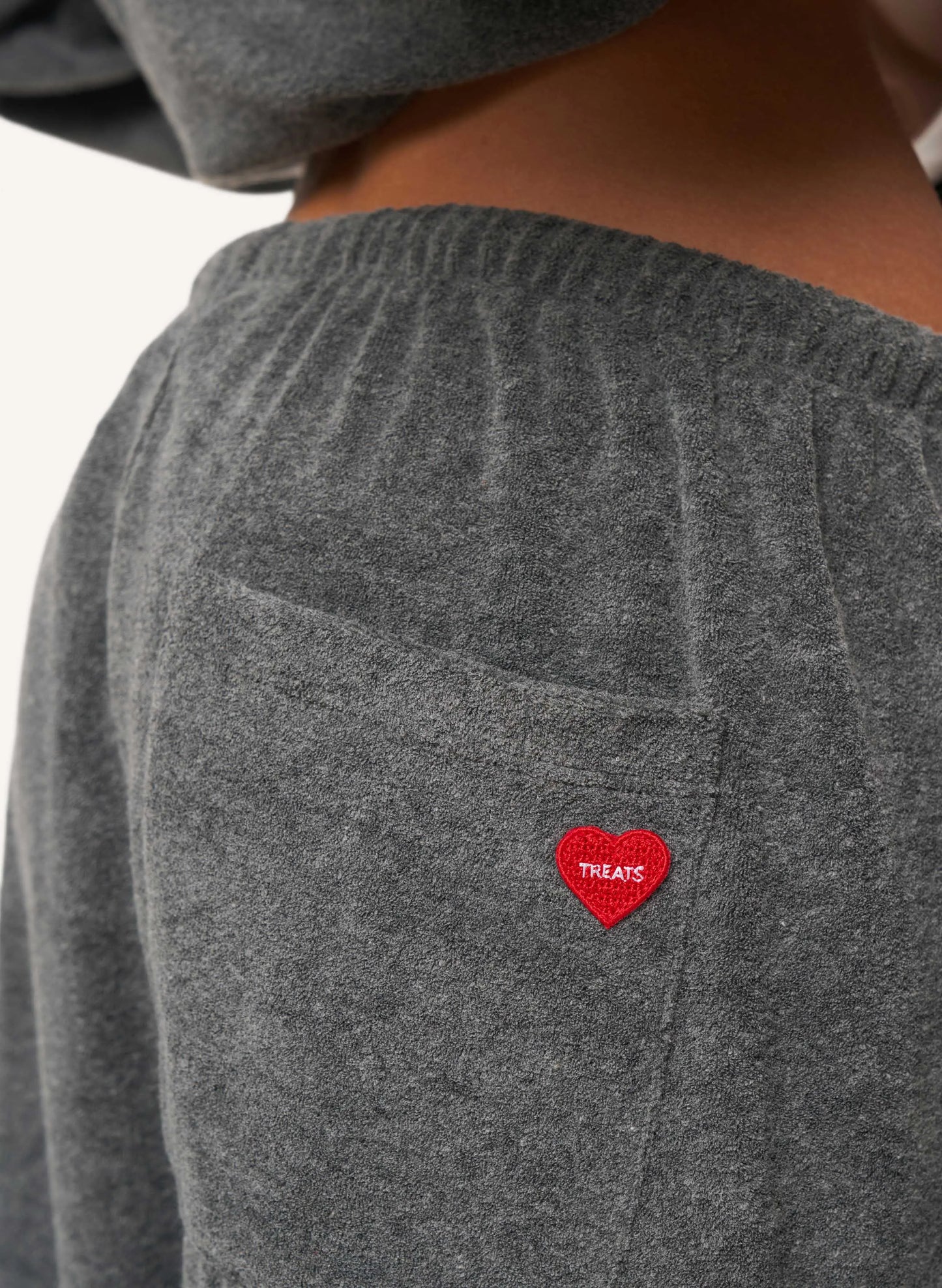 Close-up of the back of a person wearing a grey sweatpant, with a small red heart patch on the back pocket that reads 'TREATS'.