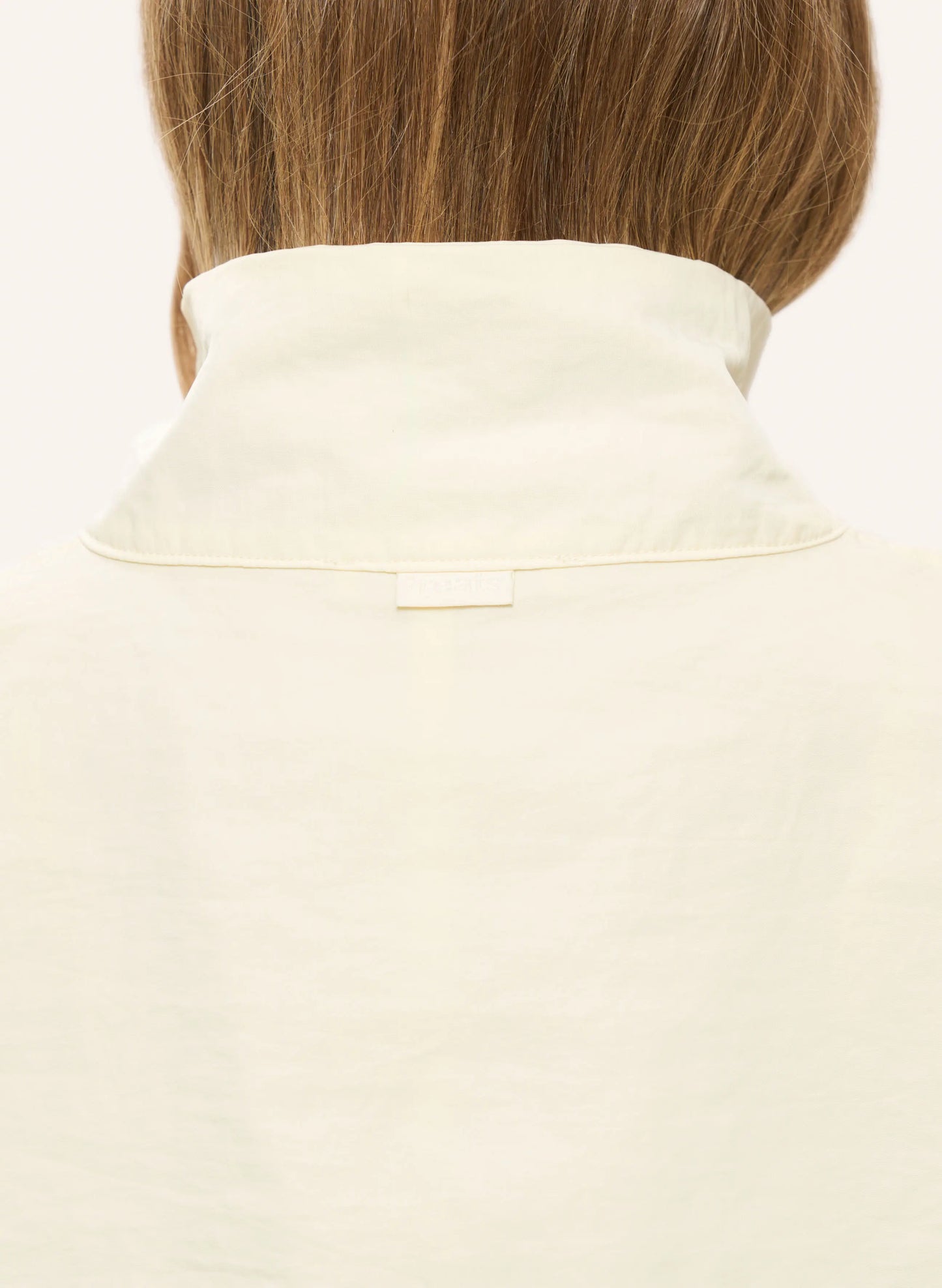 Close-up back view of a person wearing a cream-colored high collar shirt or blouse, showing the collarband and a small rectangular neck label.