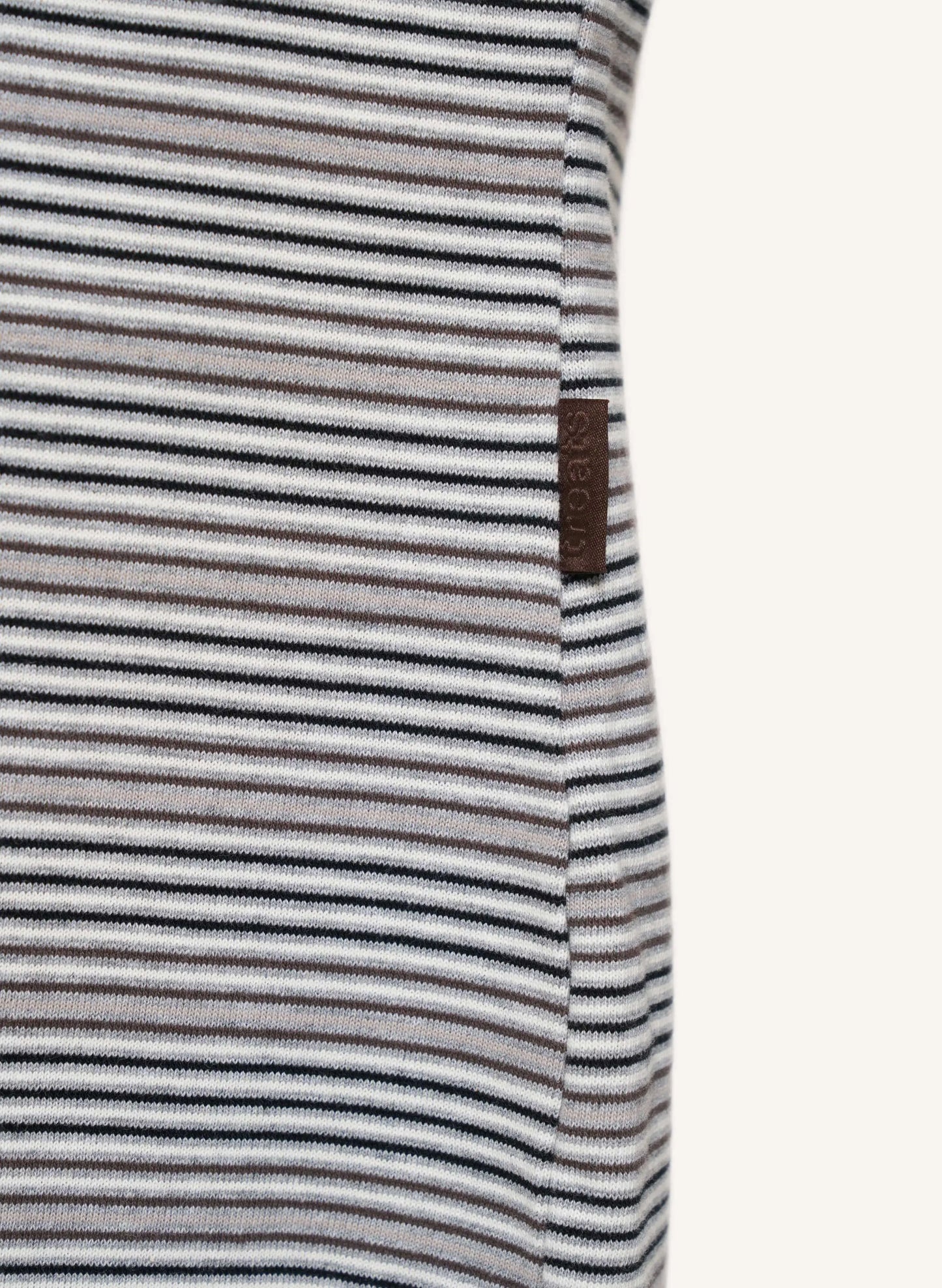 Close-up of a striped garment with thin horizontal black, gray, and white stripes, featuring a small brown brand tag on the side.