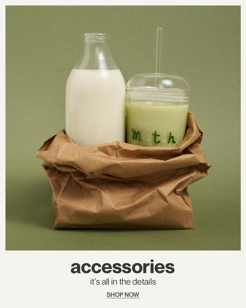 Glass bottle and cup with straw on a brown paper bag against a green background, with text 'accessories' and 'SHOP NOW'.
