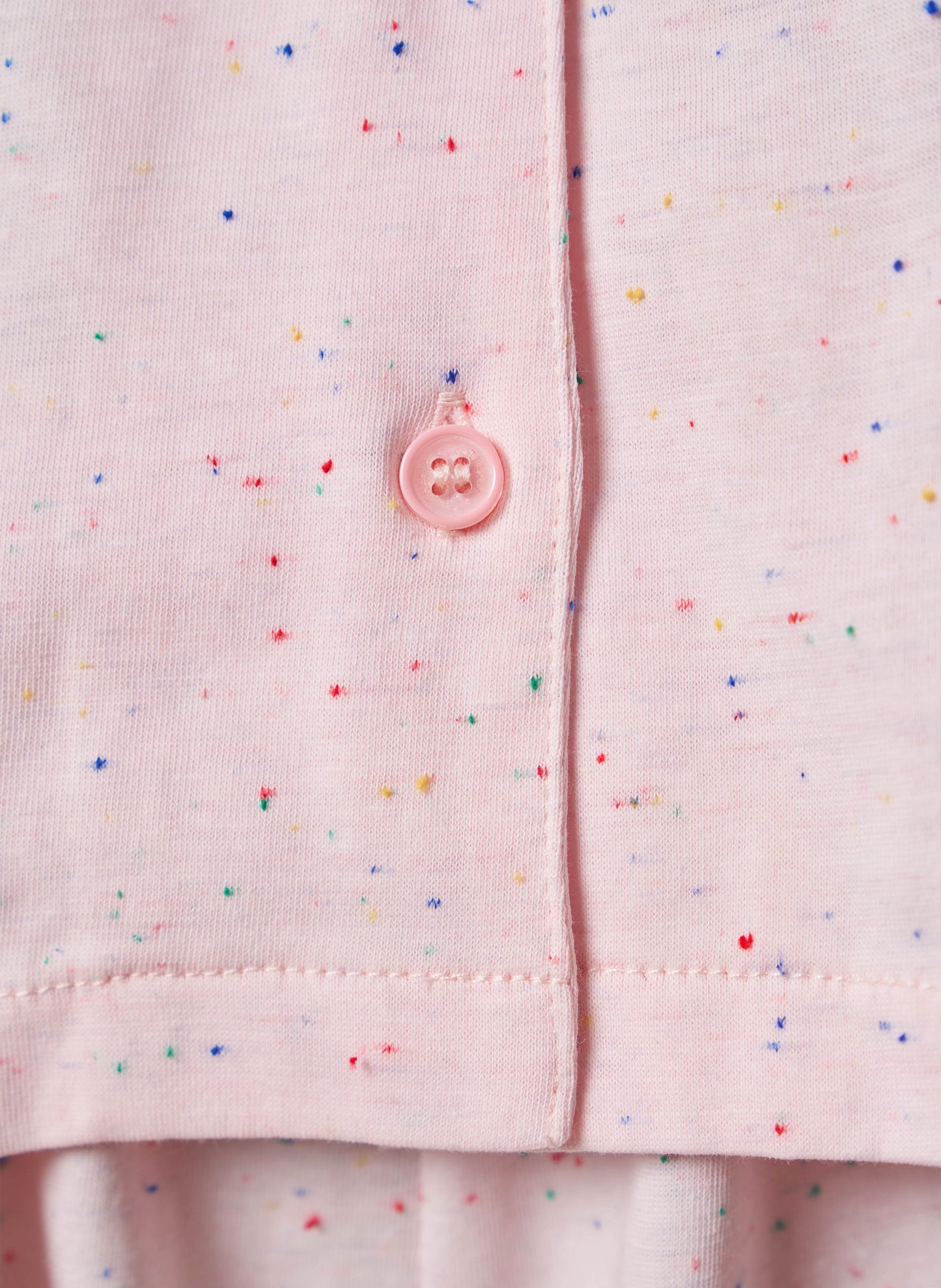 Close-up of a pink shirt with colorful speckles and a button on a matching background.