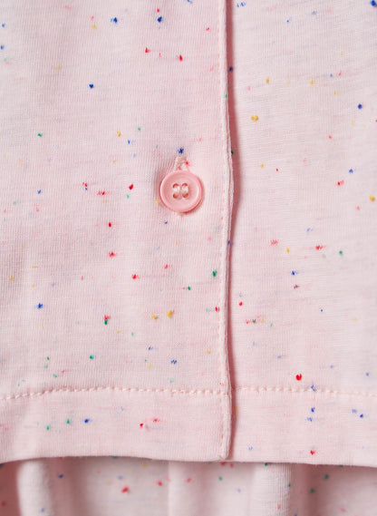 Close-up of a pink shirt with colorful speckles and a button on a matching background.