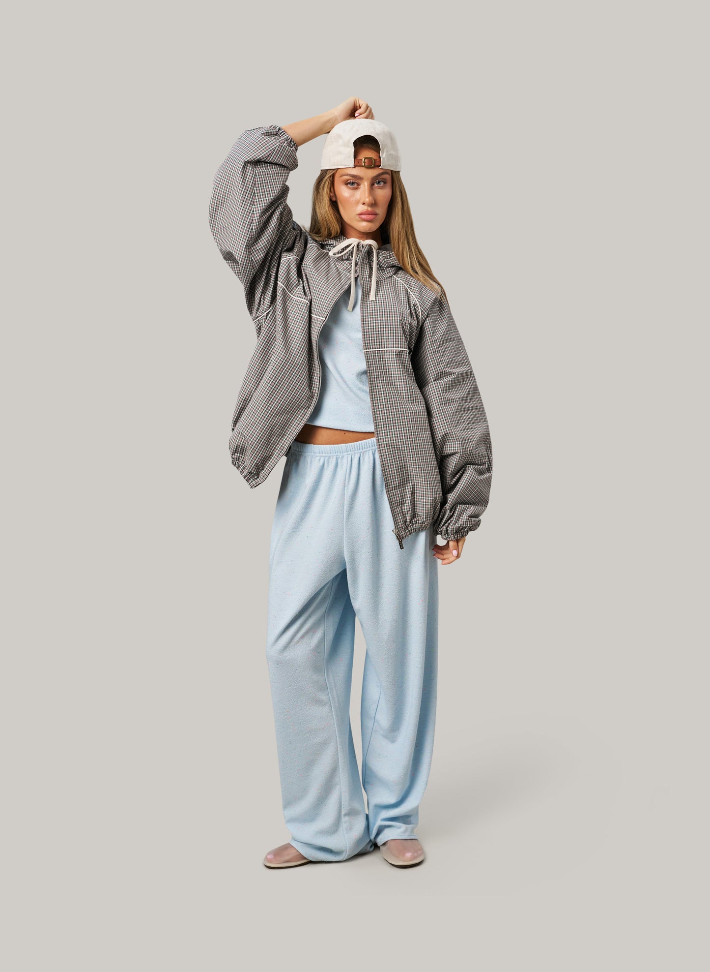 Woman wearing a gray jacket and light blue pants on a plain background