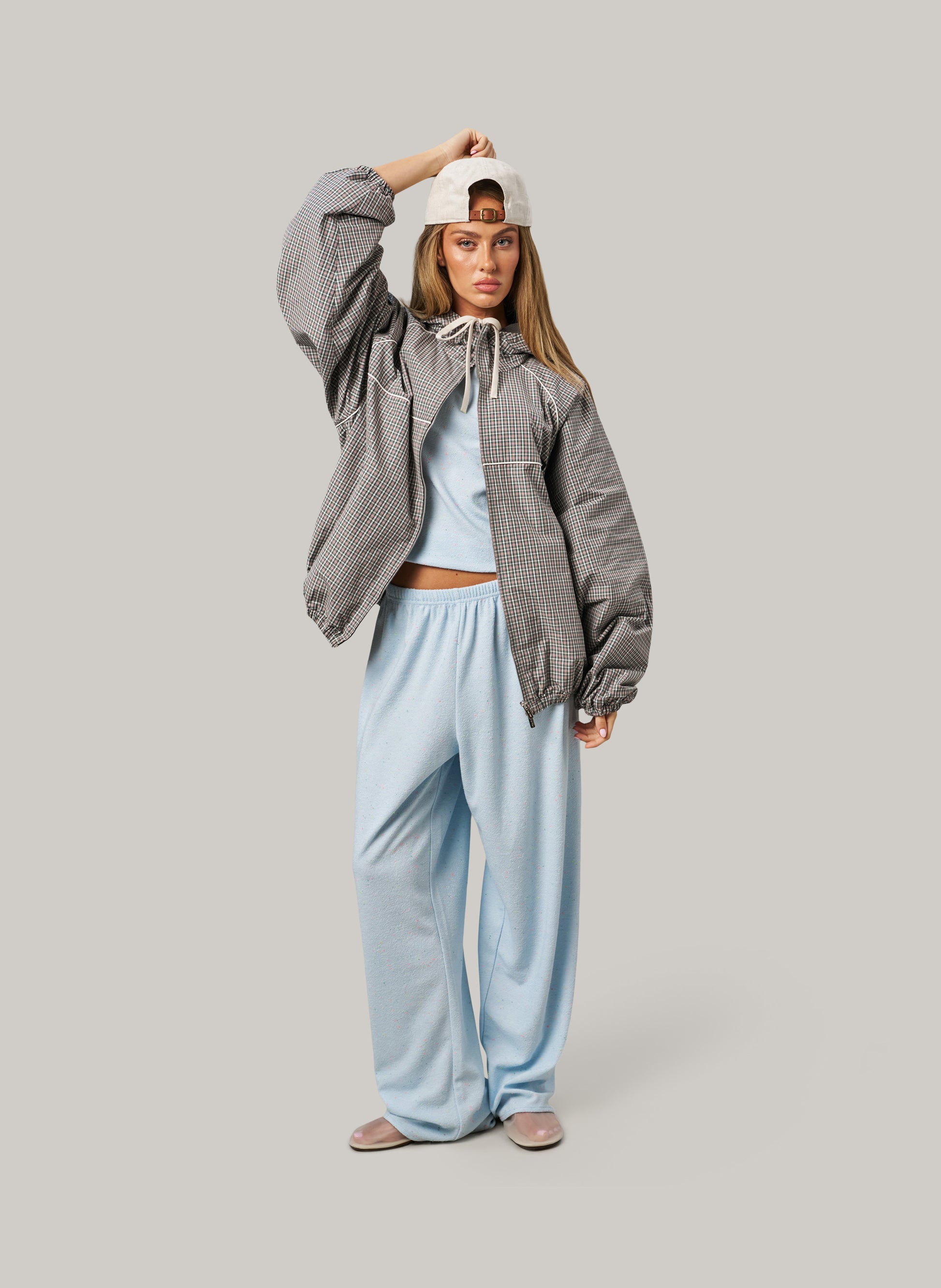 Woman wearing a gray jacket and light blue pants on a plain background