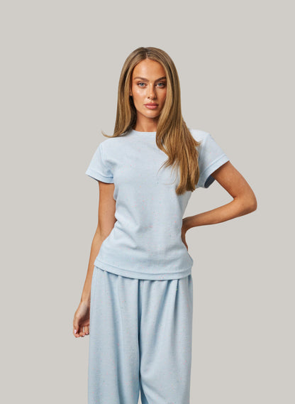 Woman wearing a light blue t-shirt and pants against a plain background