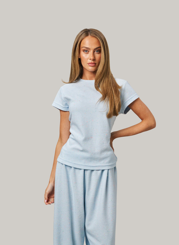 Woman wearing a light blue t-shirt and pants against a plain background