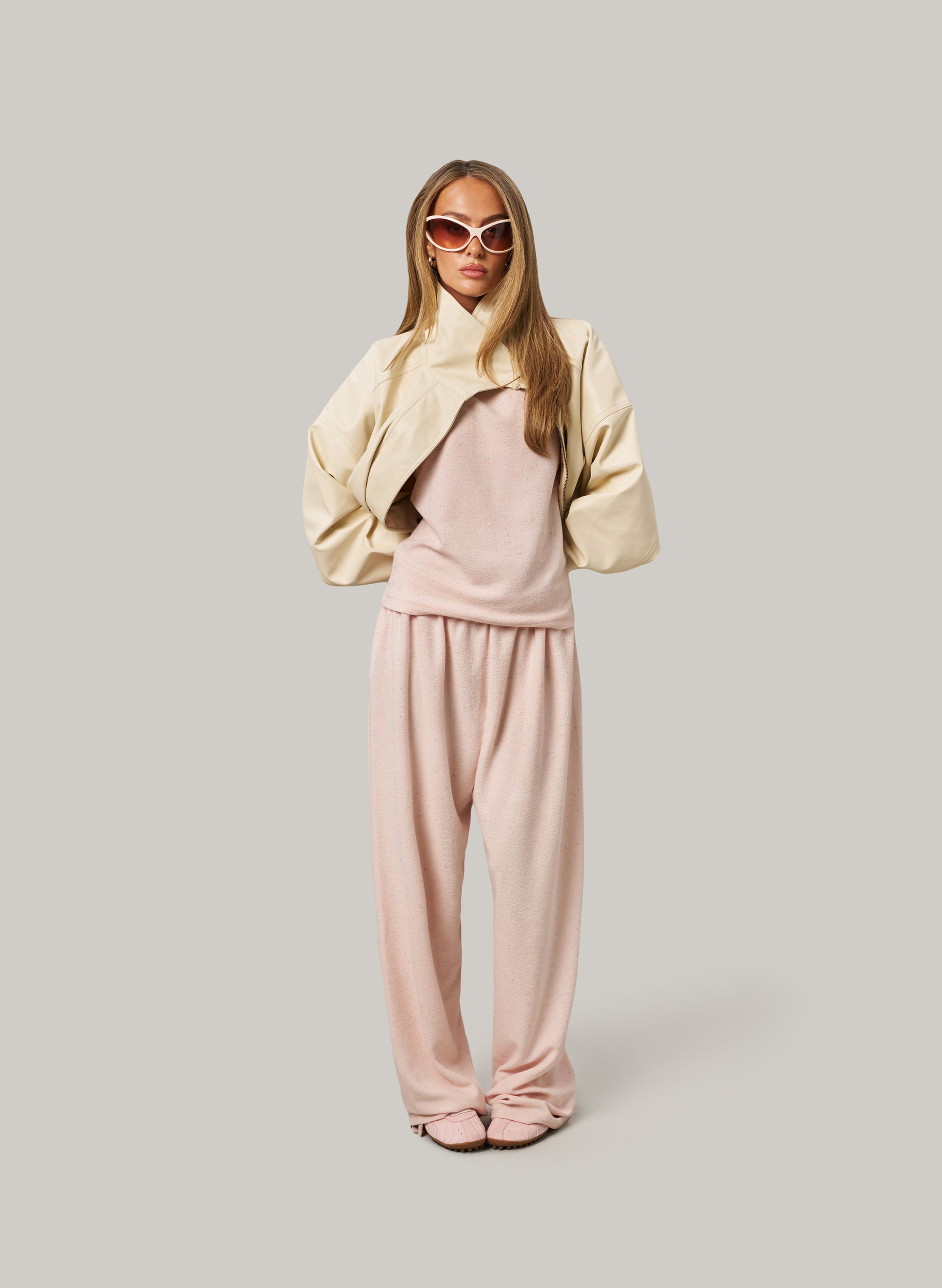 Woman wearing a beige jacket and pink pants on a plain background