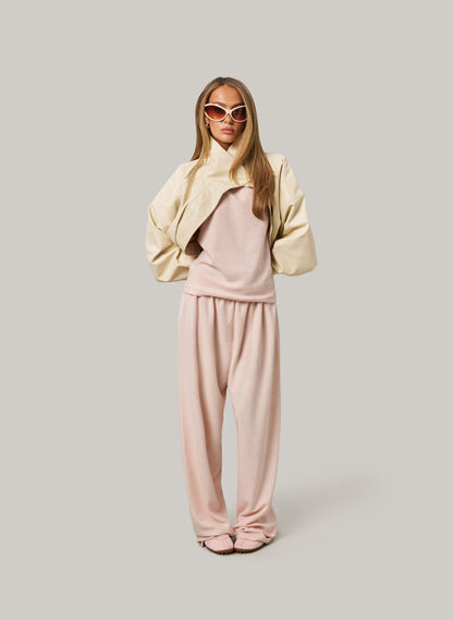 Woman wearing a beige jacket and pink pants on a plain background