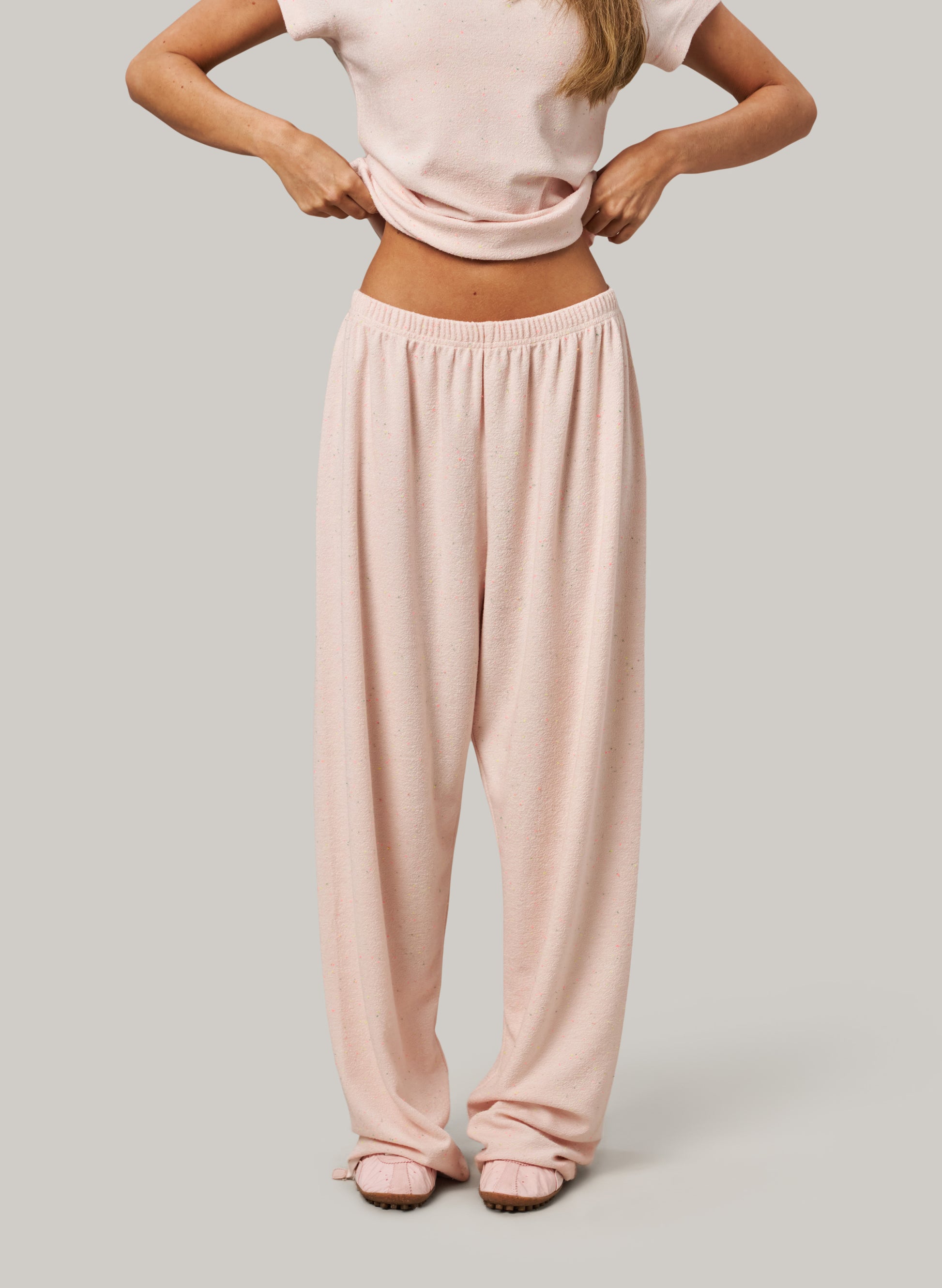 Person wearing a light pink top and matching pants on a neutral background