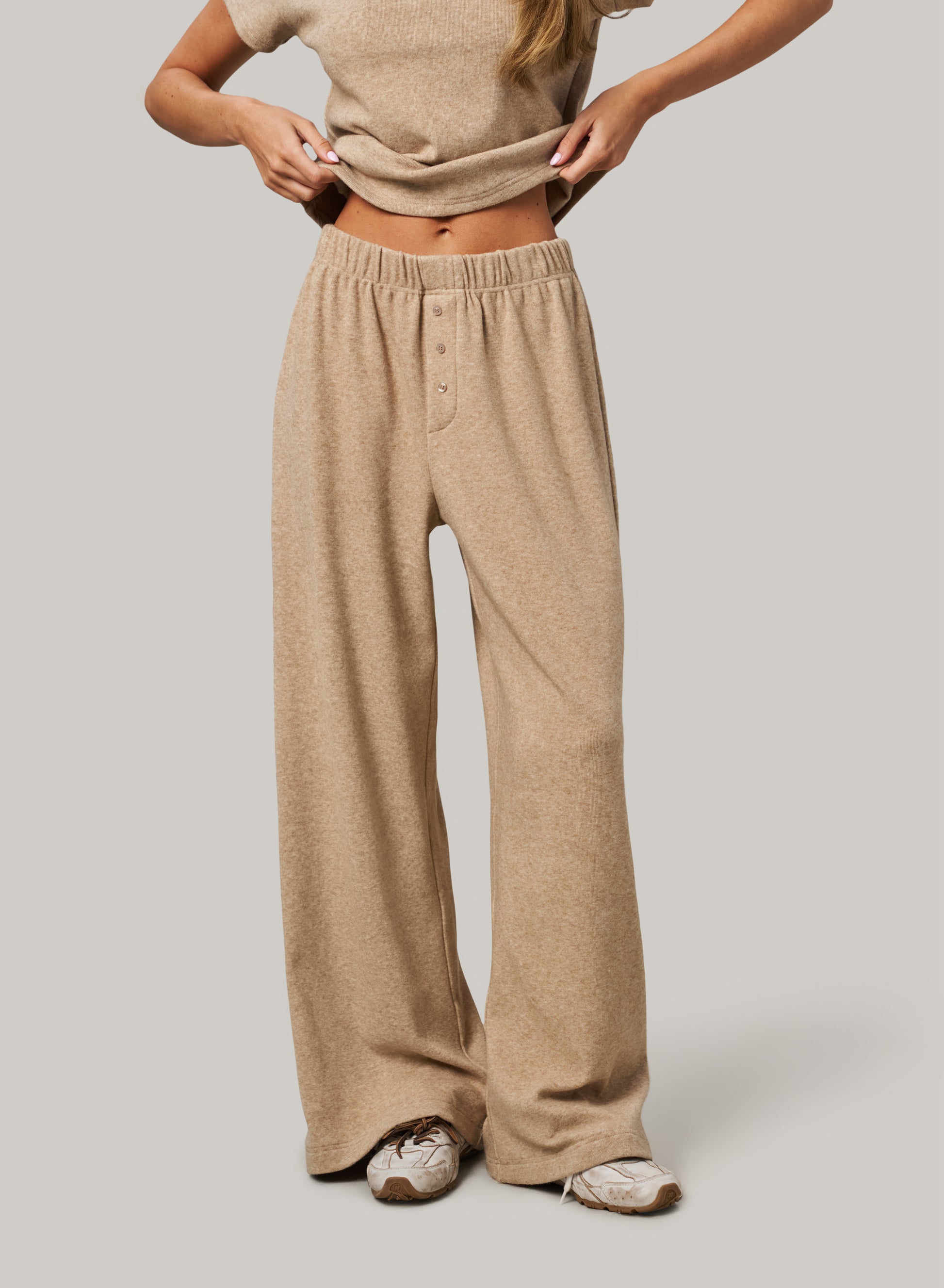 Person wearing beige lounge pants and a matching top on a plain background
