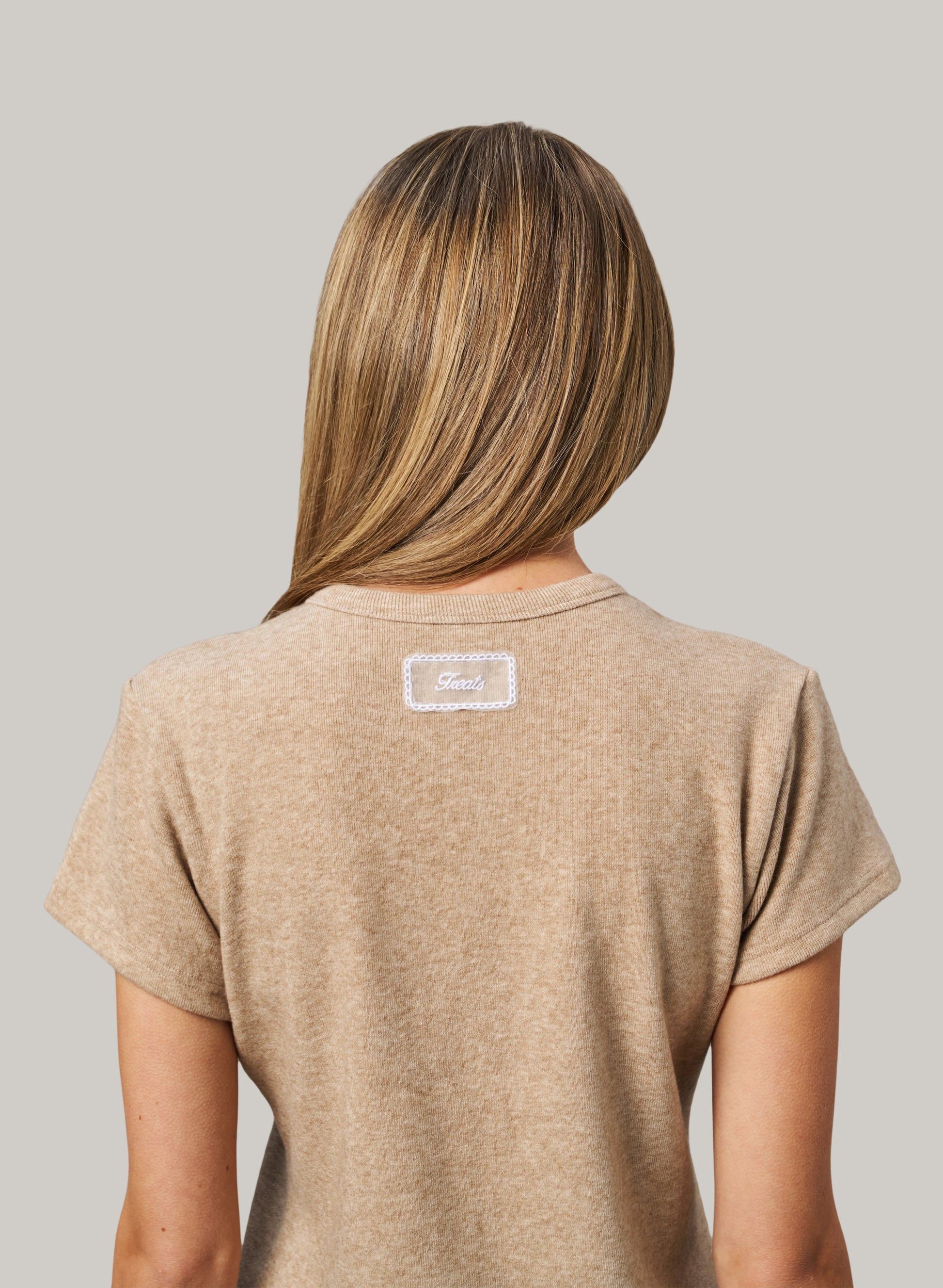Person wearing a beige t-shirt with a logo on the back against a gray background