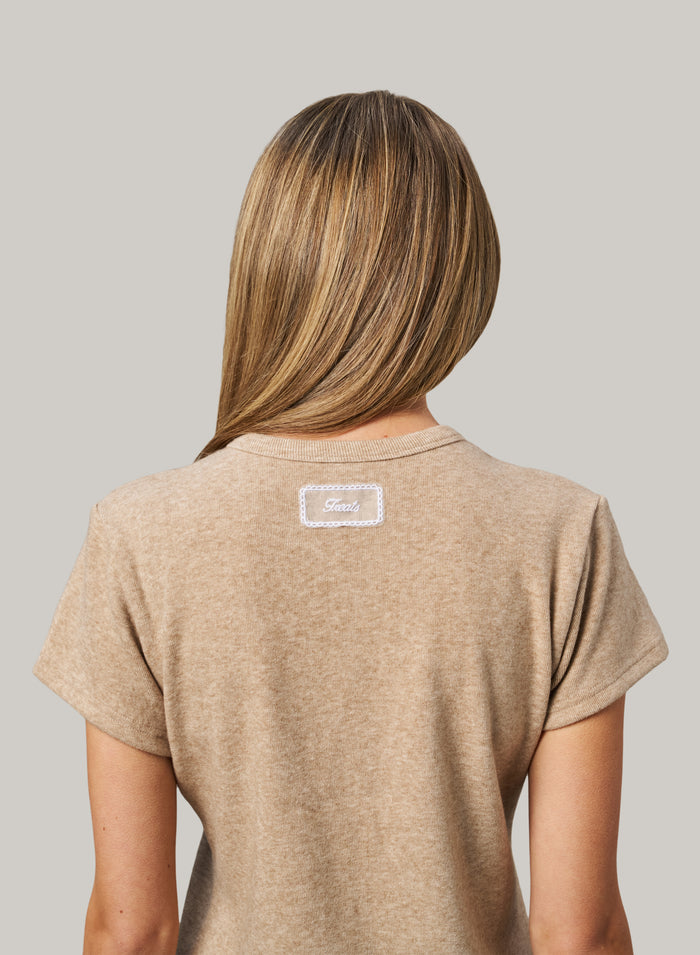 Person wearing a beige t-shirt with a logo on the back against a gray background