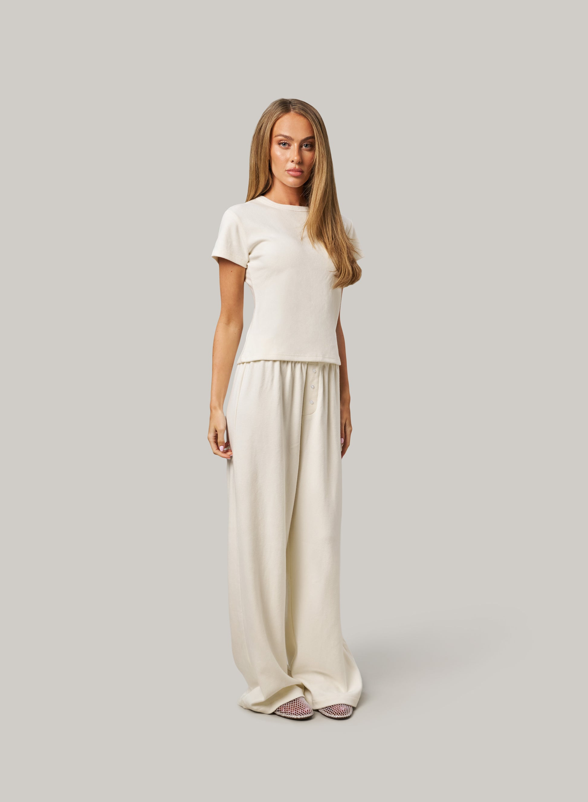 Woman wearing a white t-shirt and wide-leg pants on a gray background