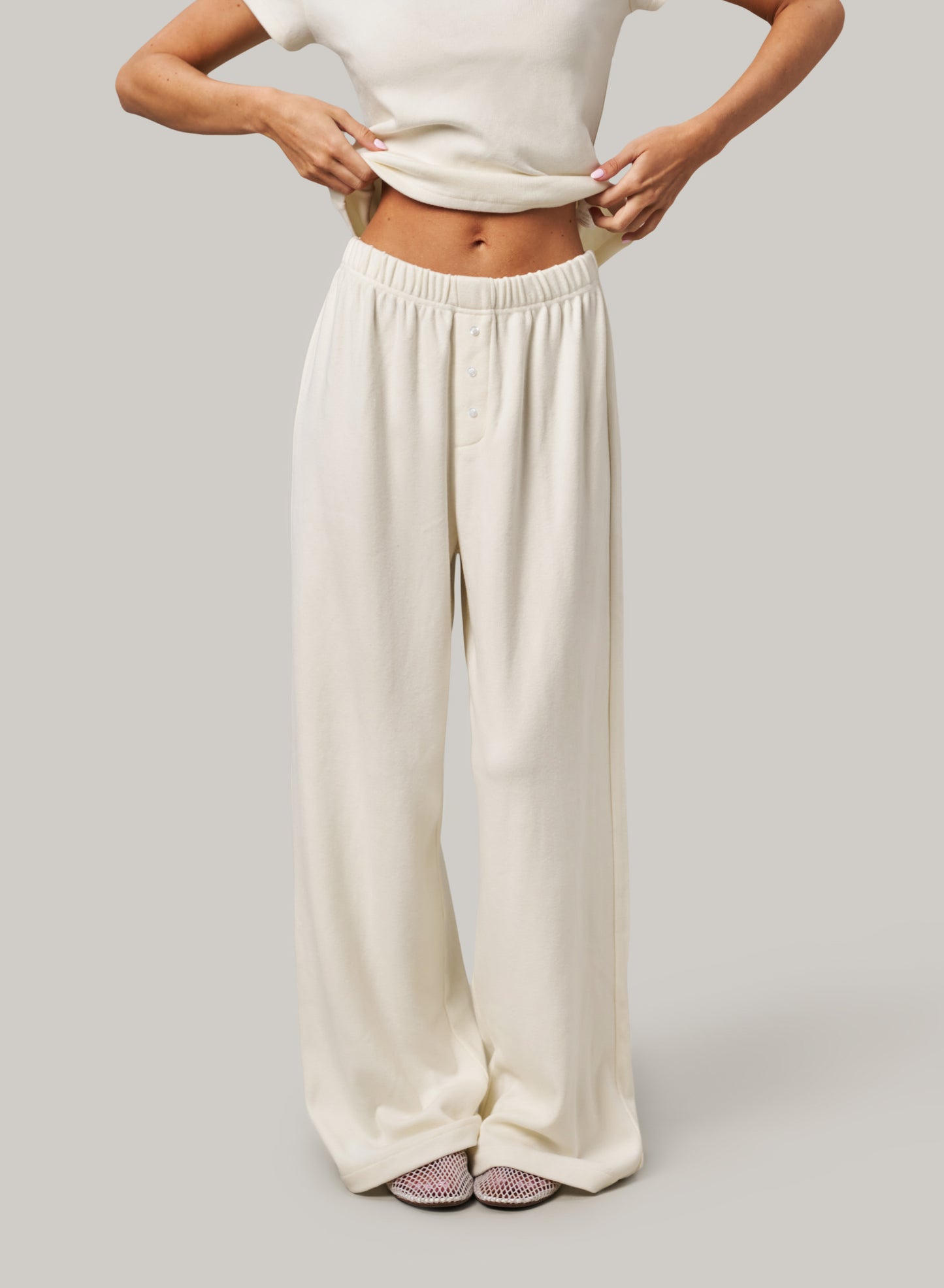 Person wearing white wide-leg pants and a white top on a light grey background