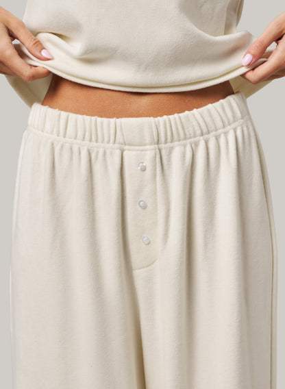 White pants with button details worn by a person on a plain background