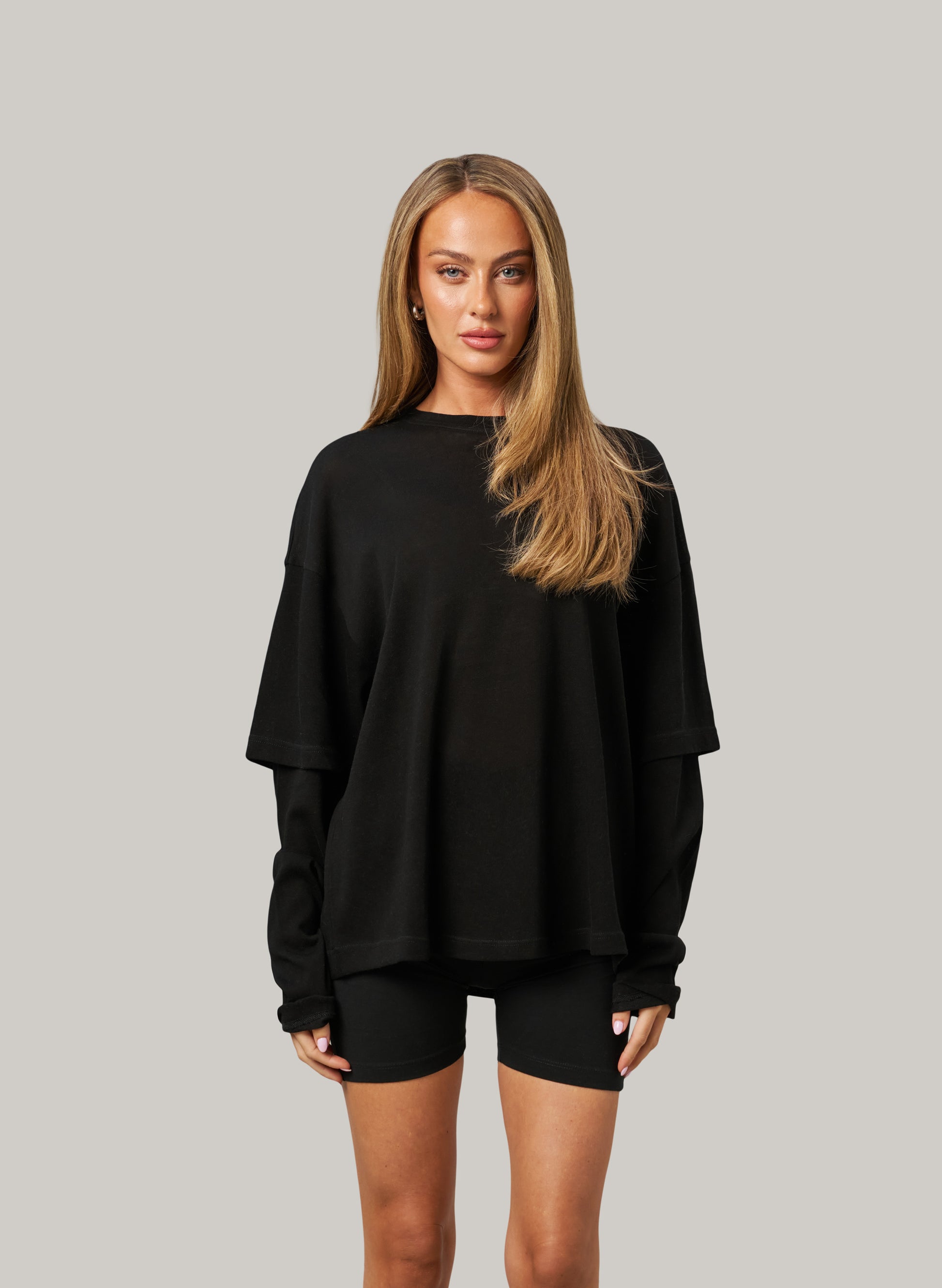 Woman wearing a black oversized sweatshirt and shorts on a gray background