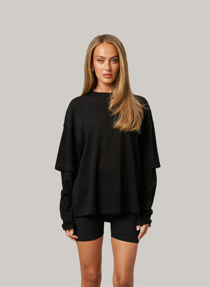 Woman wearing a black oversized sweatshirt and shorts on a gray background