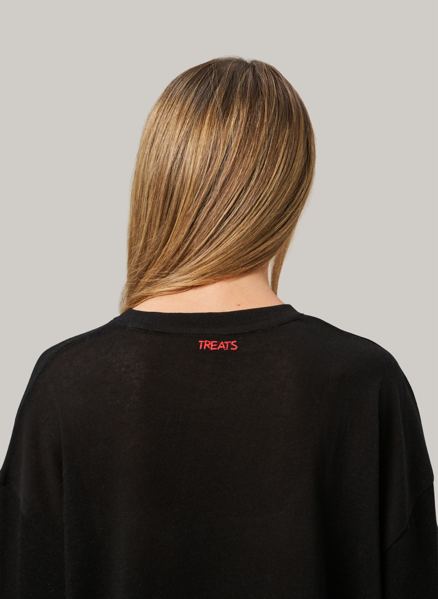 Person wearing a black sweatshirt with 'TREATS' logo on the back against a gray background