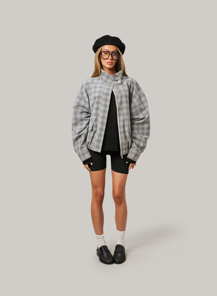 Person wearing a gray plaid jacket, black beret, and black shorts on a light gray background
