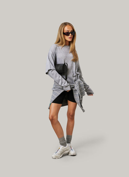 Woman wearing a gray oversized sweater with black shorts on a plain background