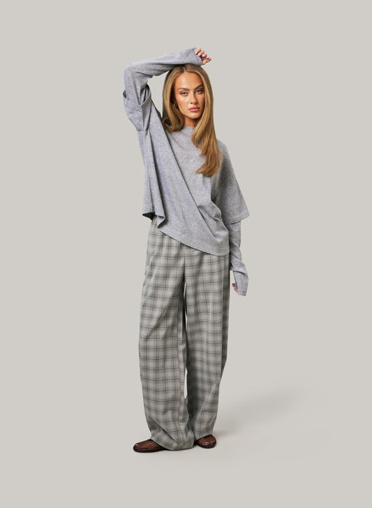 Woman wearing a gray oversized sweater and plaid pants on a light gray background