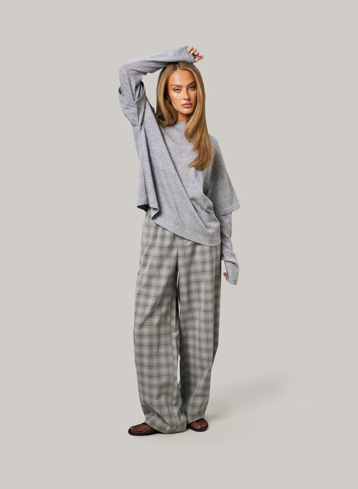 Woman wearing a gray oversized sweater and plaid pants on a light gray background