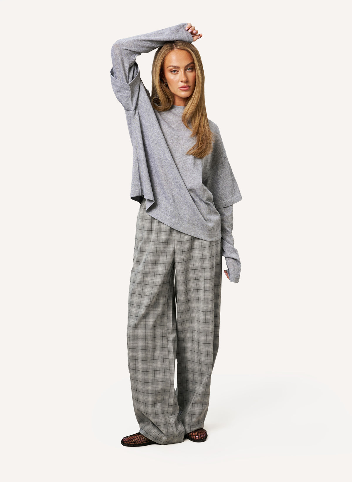 A woman modeling a gray long-sleeve knit top and wide-leg plaid trousers in a light gray studio setting.