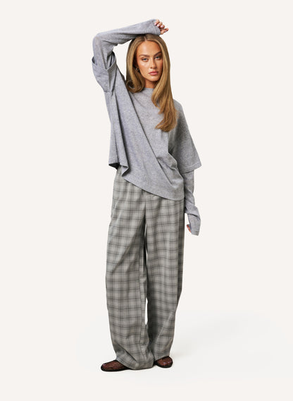 A woman modeling a gray long-sleeve knit top and wide-leg plaid trousers in a light gray studio setting.