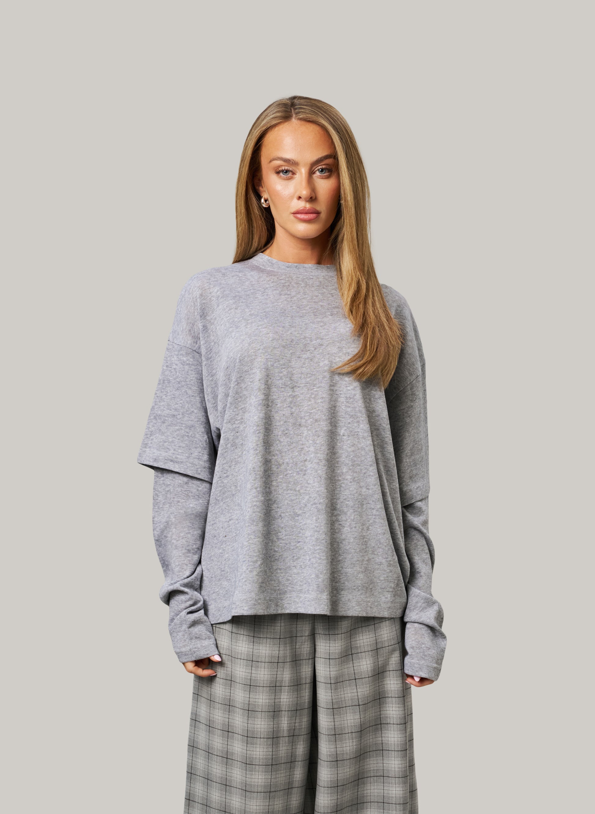 Woman wearing a gray sweater and plaid pants against a plain background