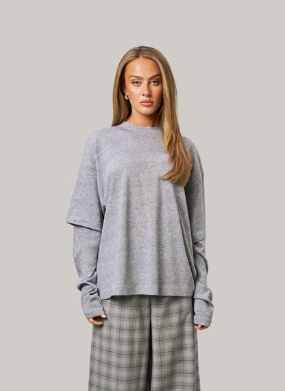 Woman wearing a gray sweater and plaid pants against a plain background