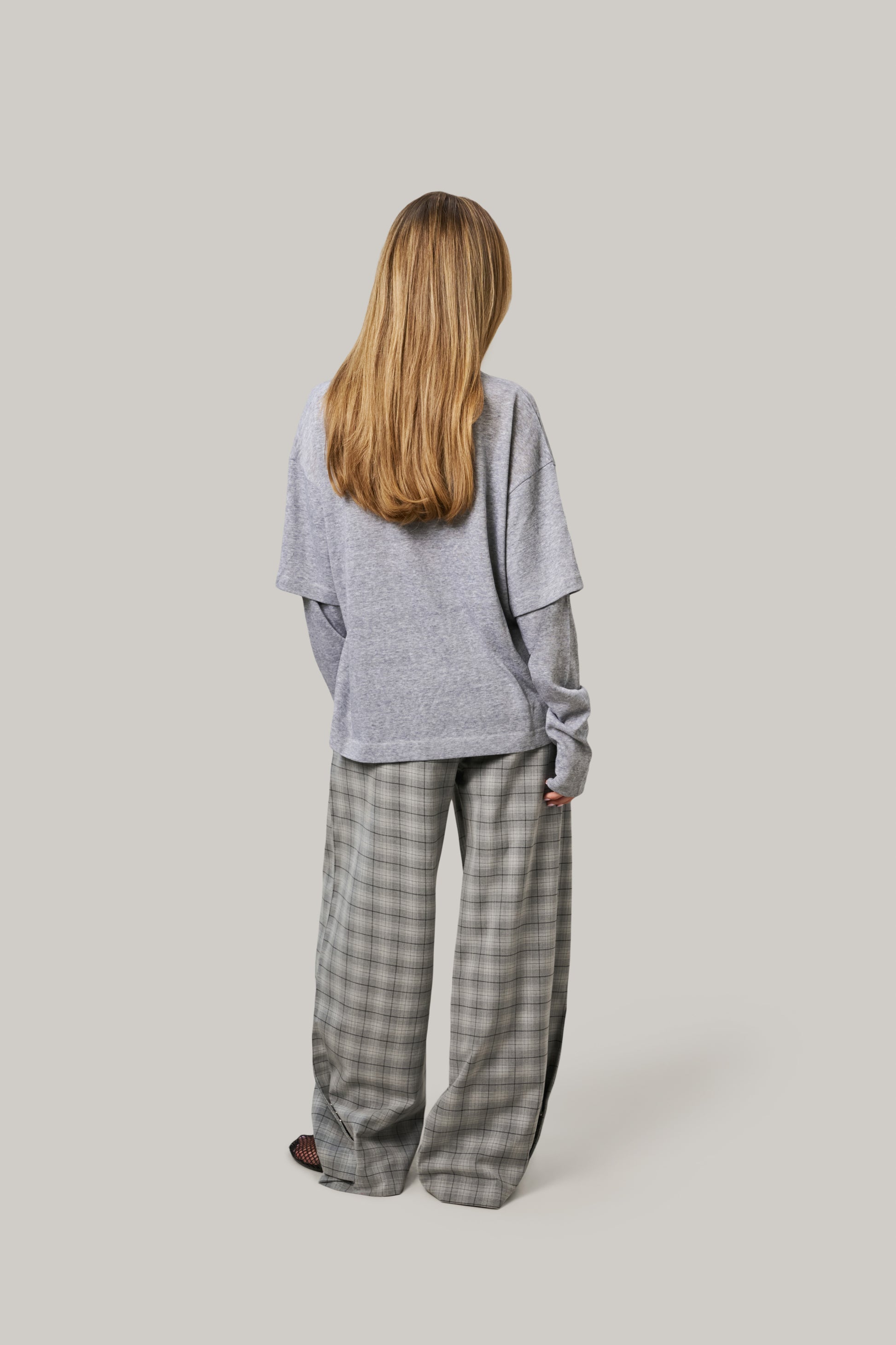 Person wearing a gray oversized top and plaid pants on a light gray background