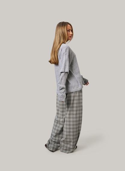 Woman wearing a gray sweater and plaid pants on a plain background