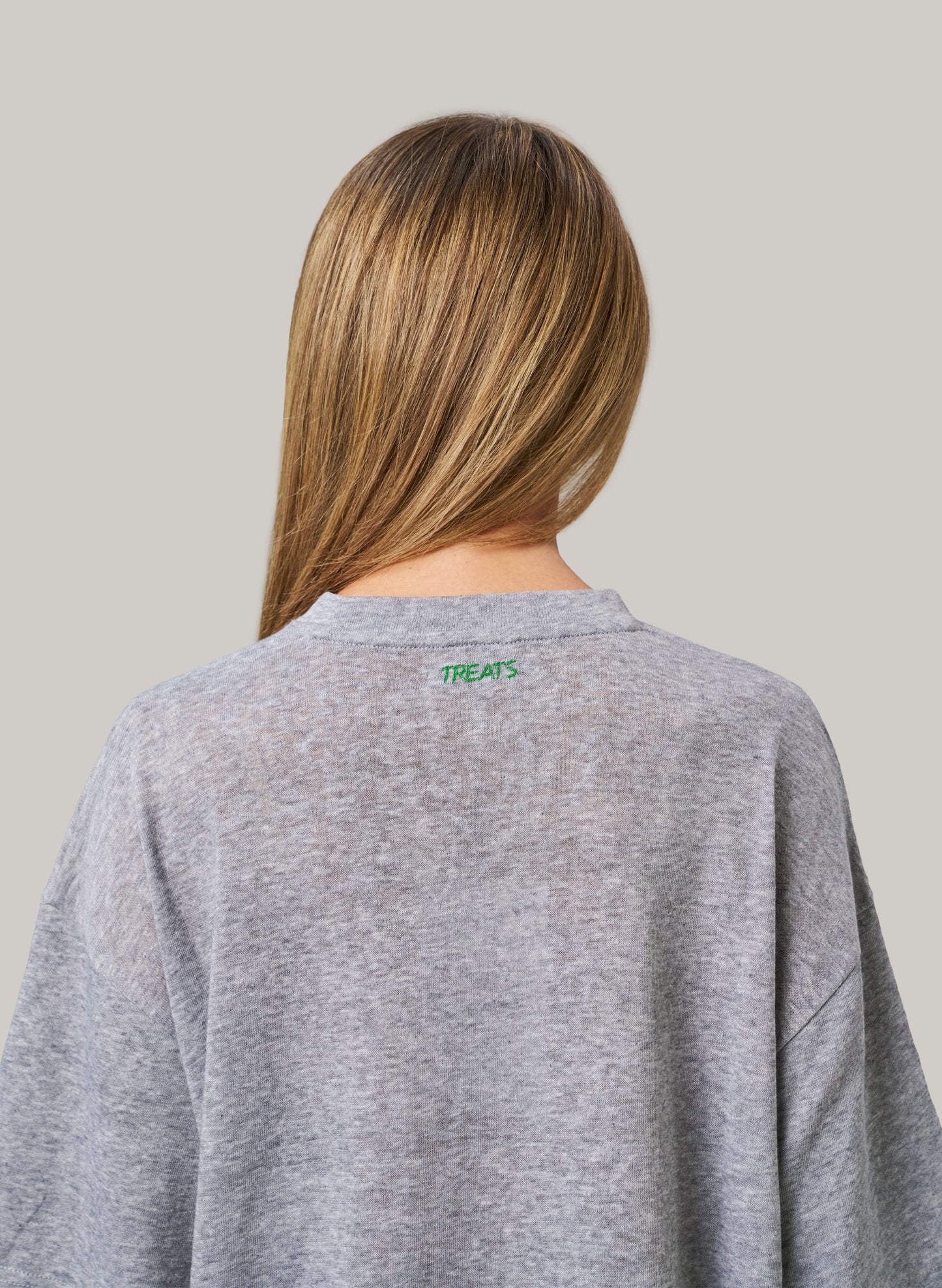 Person wearing a gray sweatshirt with 'TREATS' logo on the back against a plain background