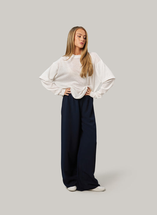 Woman wearing a white blouse and navy pants on a gray background