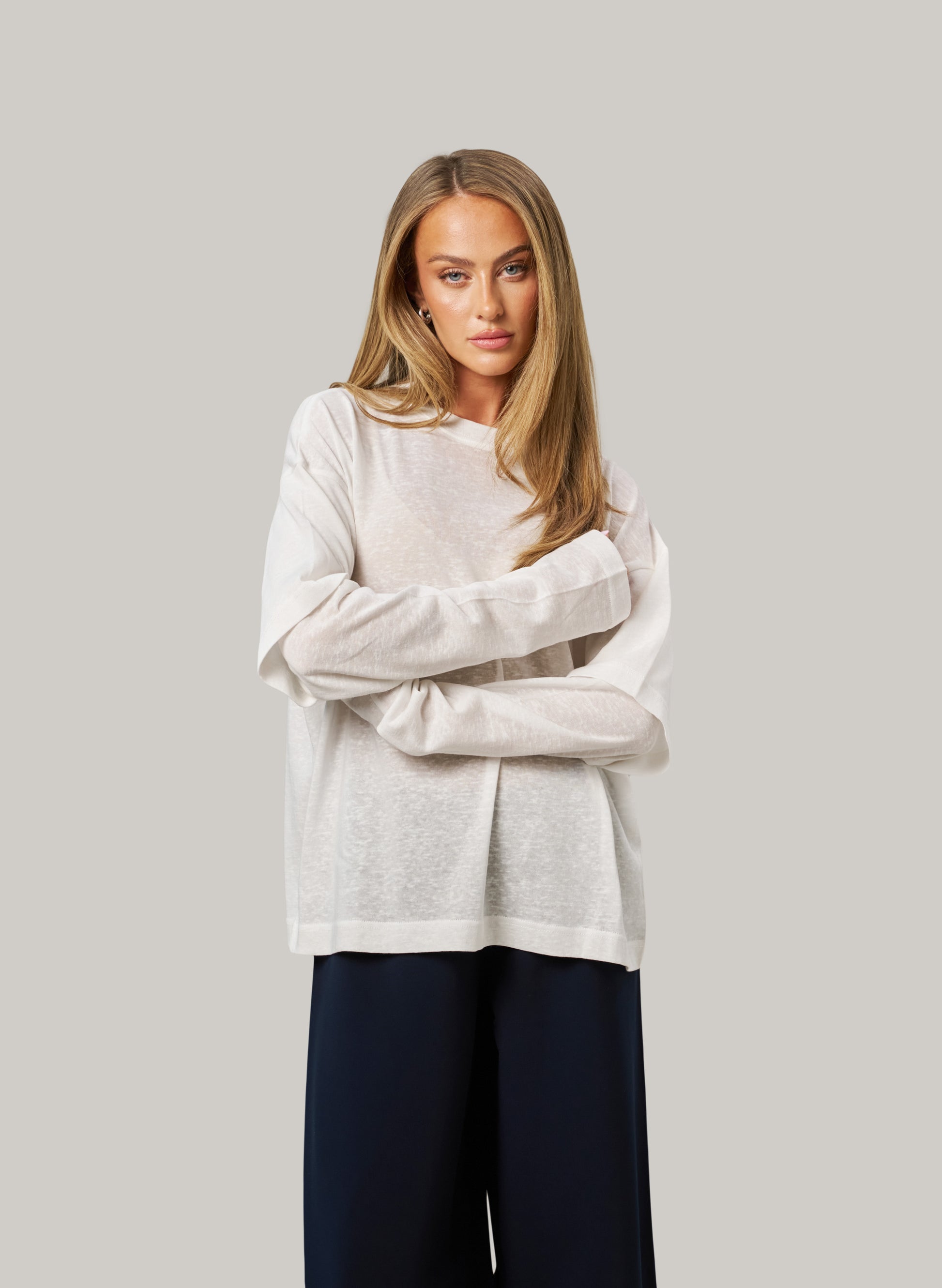 Woman wearing a white sweater and dark pants against a plain background