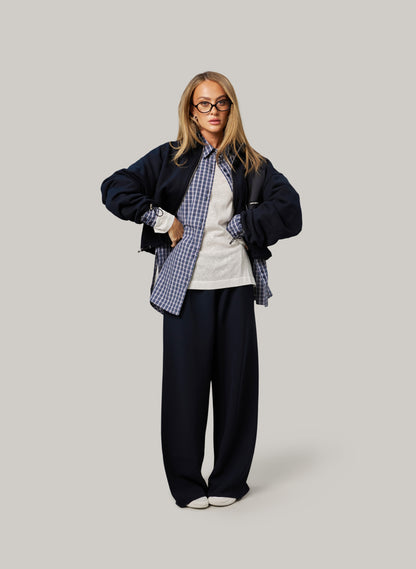 Person wearing a navy jacket, plaid shirt, and black pants on a light gray background