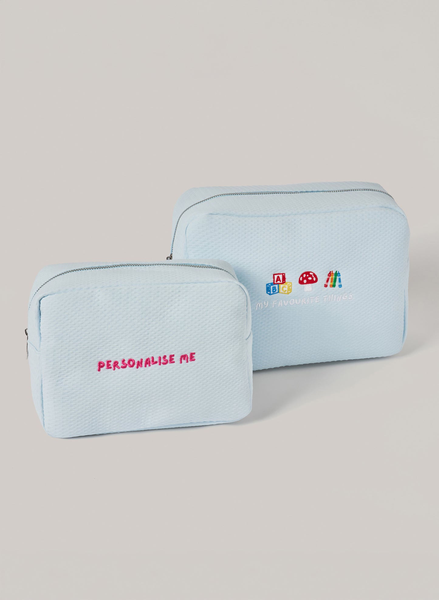 Light blue personalized toiletry bags set with embroidered “PERSONALISE ME” text on the small pouch and “MY FAVOURITE THINGS” with playful icons on the larger pouch