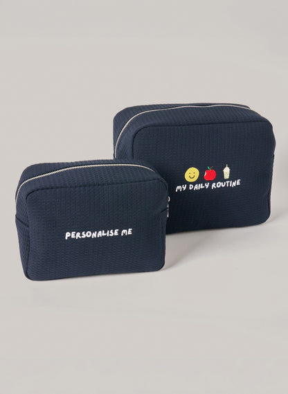 Two navy waffle-textured pouches with zipper closures, one featuring ‘personalise me’ text and the other with embroidered icons and ‘my daily routine’ text on the front.