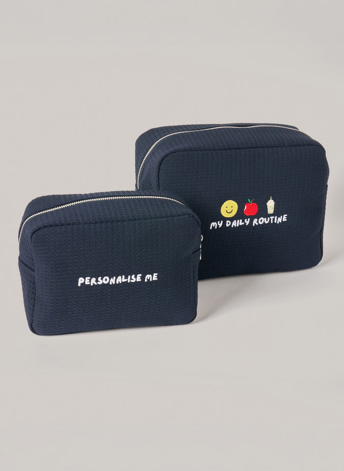 Two navy waffle-textured pouches with zipper closures, one featuring ‘personalise me’ text and the other with embroidered icons and ‘my daily routine’ text on the front.