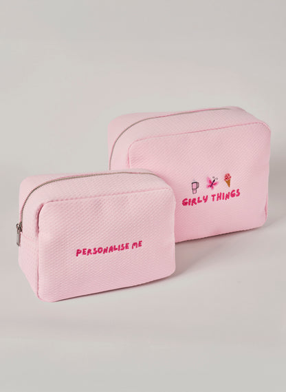 Two light pink waffle-textured pouches with zipper closures, one featuring ‘personalise me’ text and the other with embroidered icons and ‘girly things’ text on the front