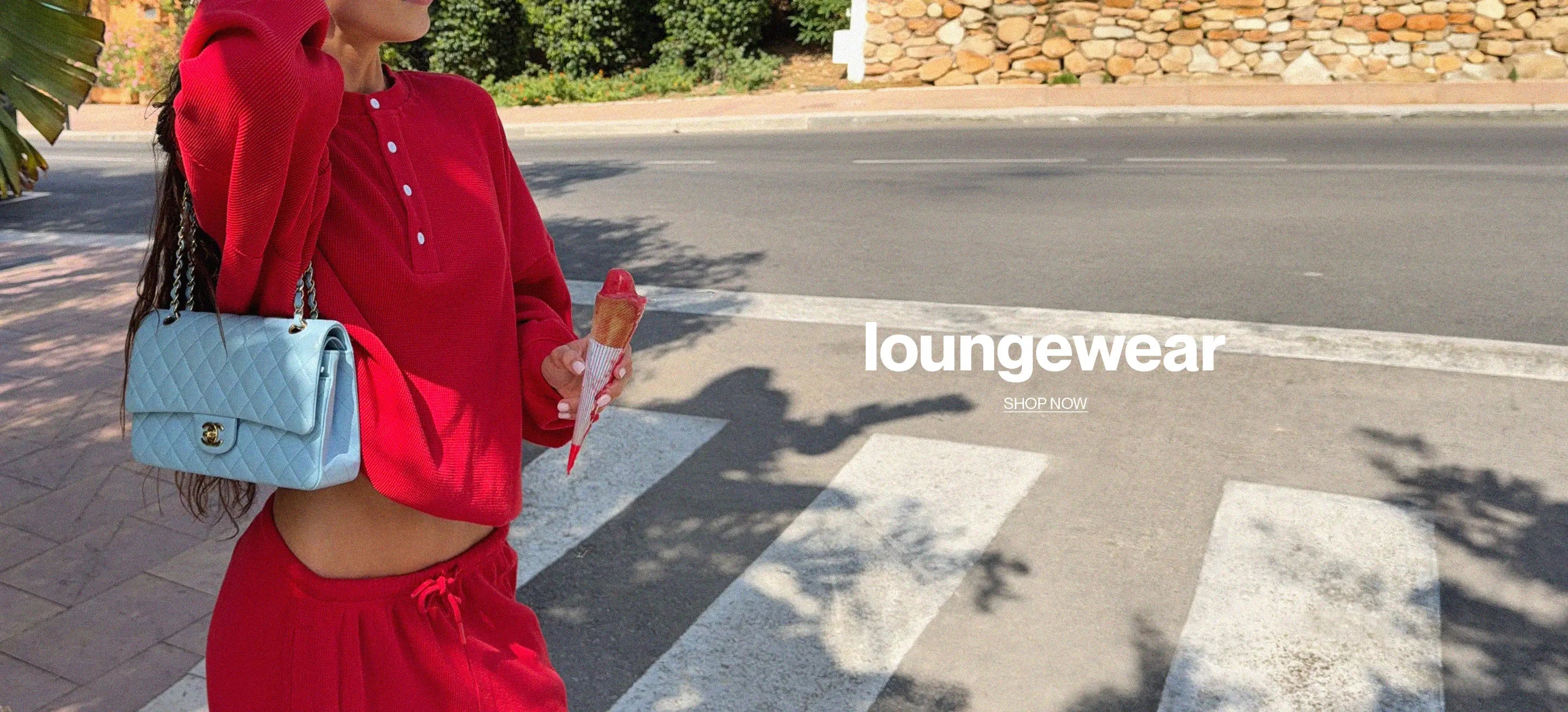 A woman wearing a matching red lounge set walks across a crosswalk outdoors, carrying a light blue quilted shoulder bag. The image features a 'loungewear' text overlay on the right side.