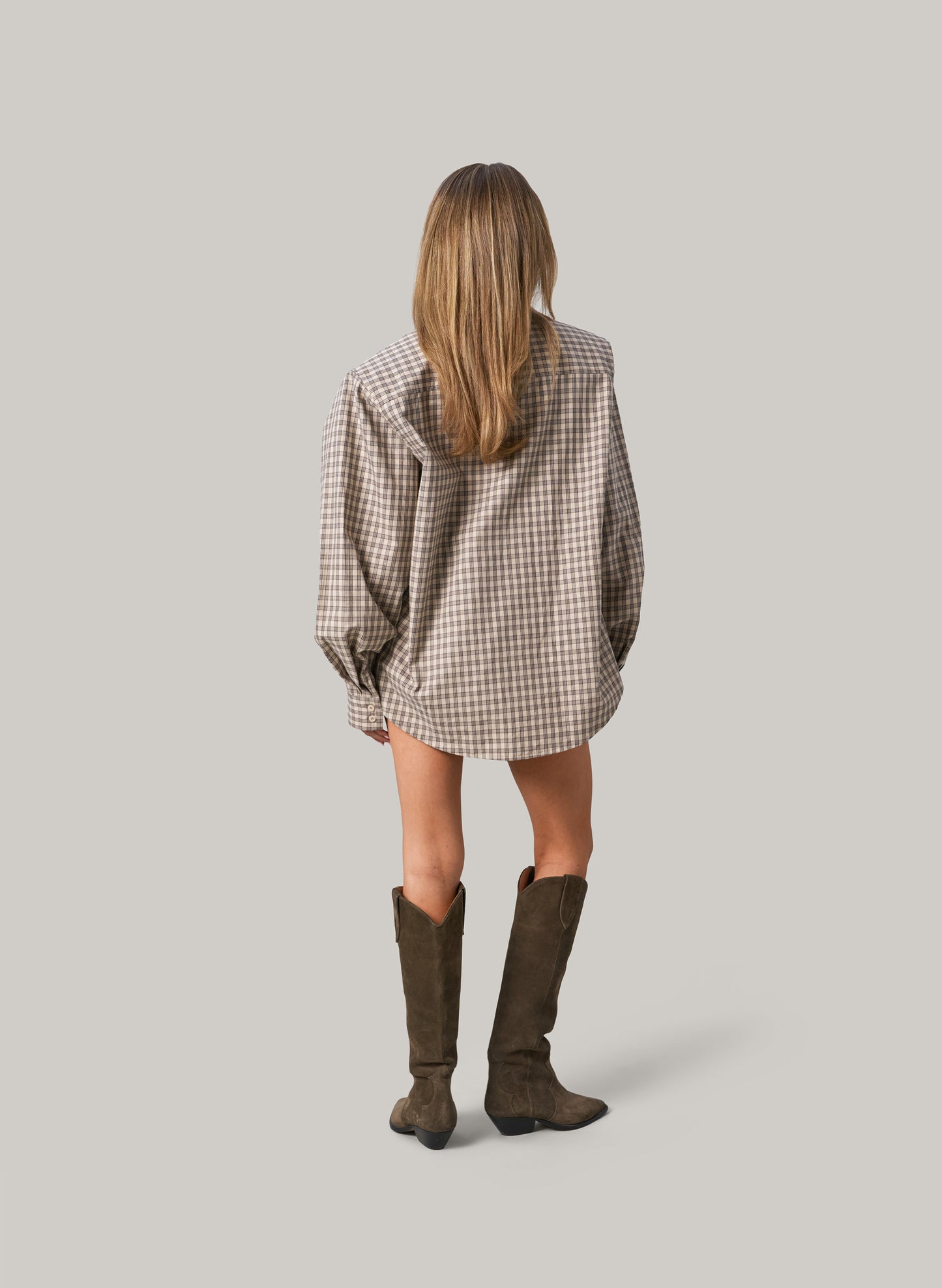 Person wearing a plaid dress and brown boots on a plain background