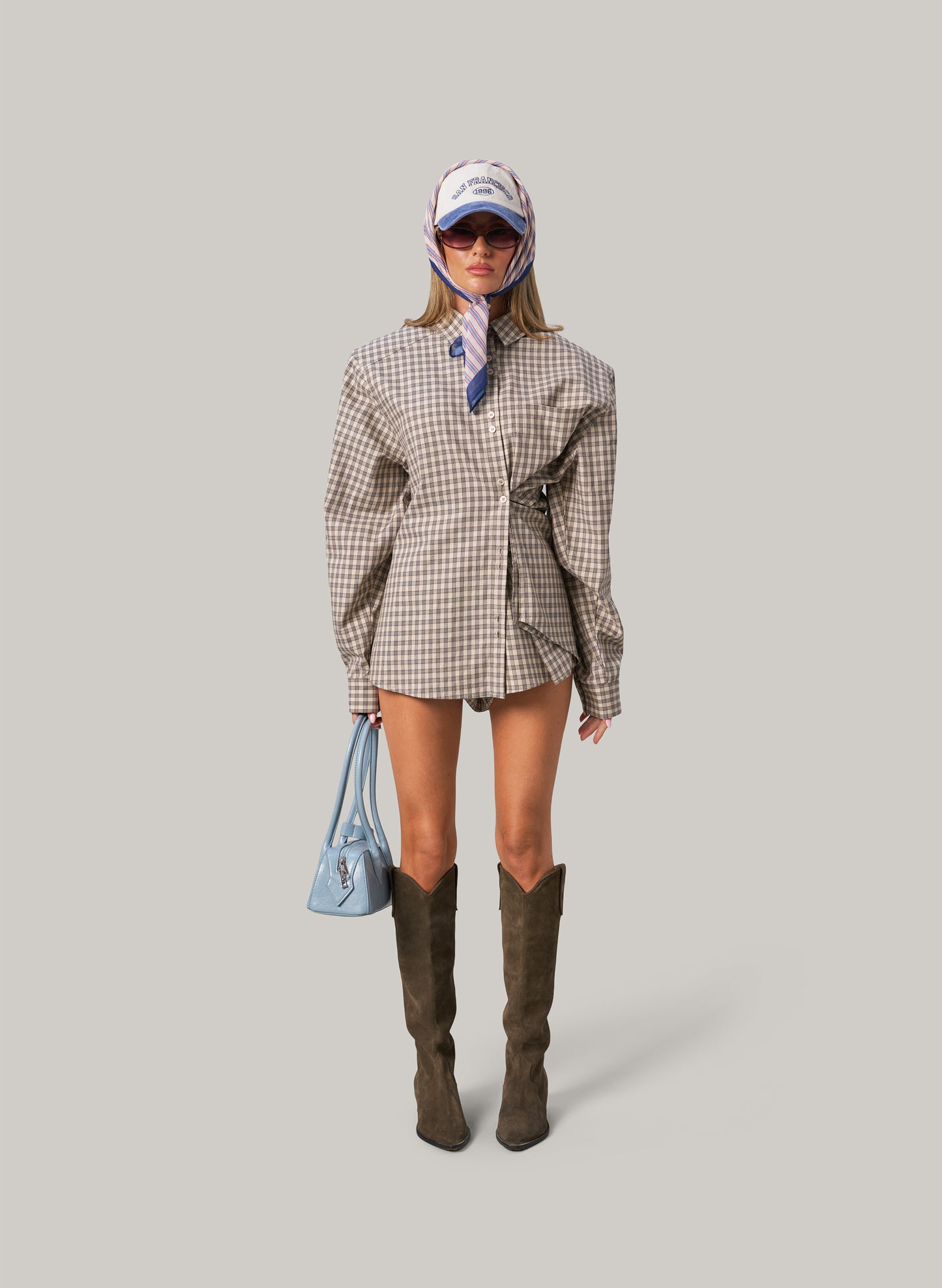 Person wearing a plaid outfit with knee-high boots on a gray background
