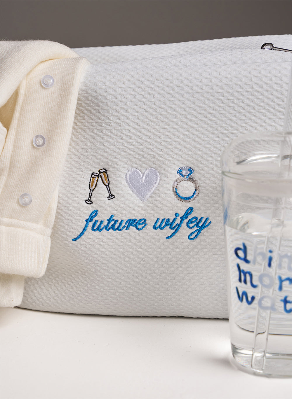 women's white set with white waffle bag with embroidery saying 'future wifey' on. Stood up next to it a glass saying 'drink more water'