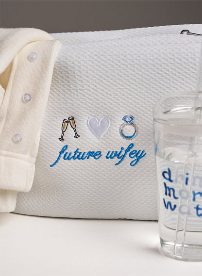 women's white set with white waffle bag with embroidery saying 'future wifey' on. Stood up next to it a glass saying 'drink more water'