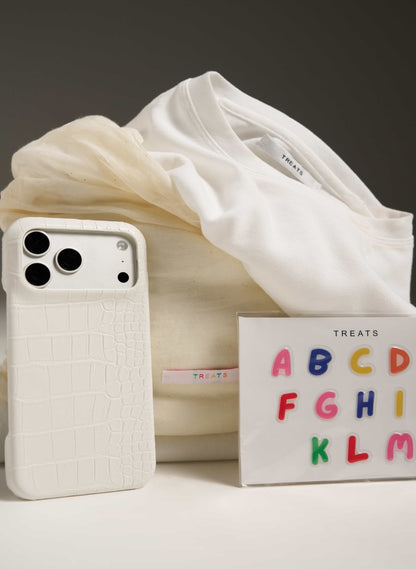 White textured phone case next to a box with colorful letters on a neutral background