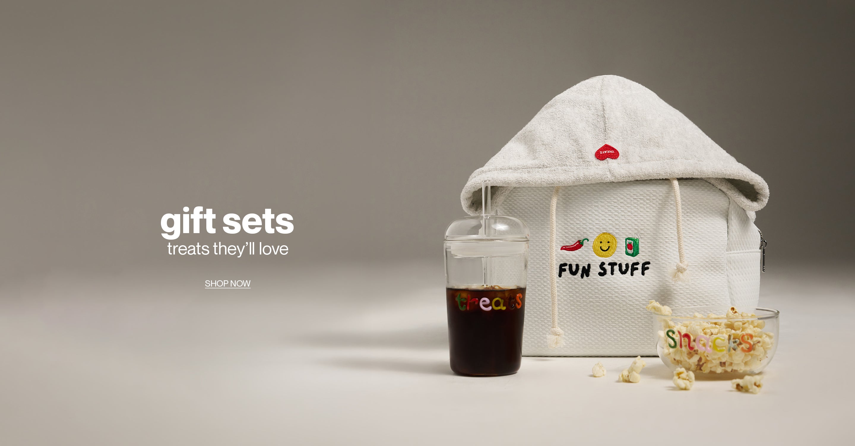 Gift set with a hoodie, glass of soda, and bowl of popcorn on a neutral background.